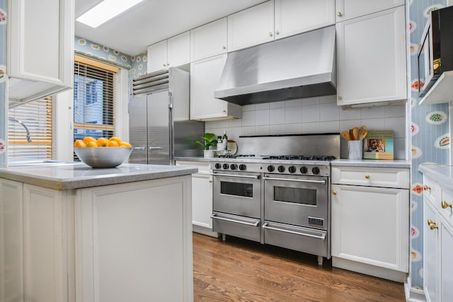 kitchen featuring decorative backsplash, premium appliances, wood finished floors, under cabinet range hood, and white cabinetry