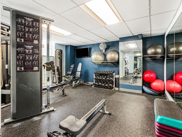 exercise room featuring a paneled ceiling and baseboards