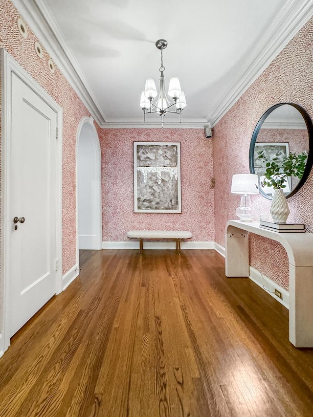 unfurnished dining area featuring arched walkways, wallpapered walls, crown molding, and wood finished floors