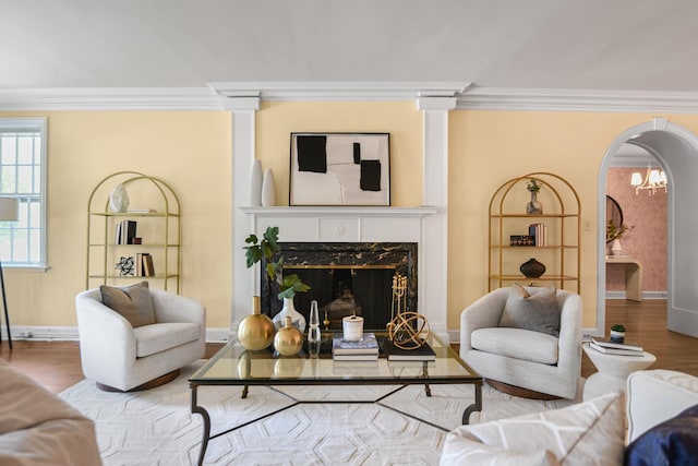 living room featuring baseboards, arched walkways, a premium fireplace, ornamental molding, and wood finished floors