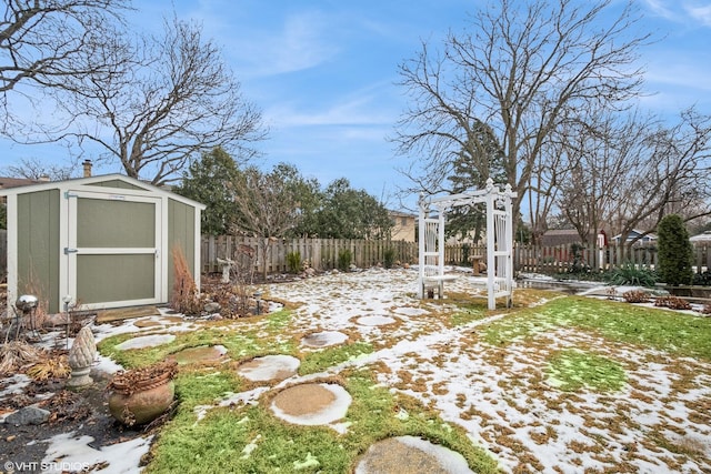 snowy yard with a shed, fence, and an outbuilding