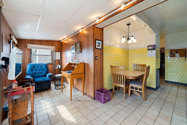 dining room with light tile patterned floors, wood walls, and a chandelier