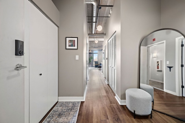 corridor with a high ceiling, baseboards, and dark wood-type flooring