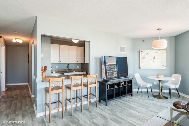 kitchen with a textured ceiling, wood finished floors, visible vents, baseboards, and white cabinetry