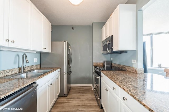 kitchen with stainless steel appliances, wood finished floors, white cabinetry, a sink, and light stone countertops