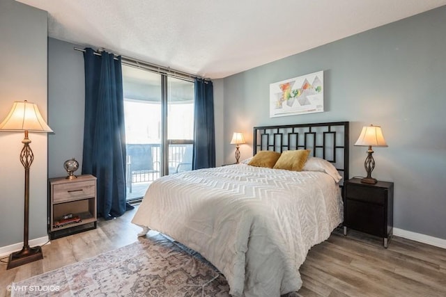 bedroom featuring access to outside, a wall of windows, wood finished floors, and baseboards