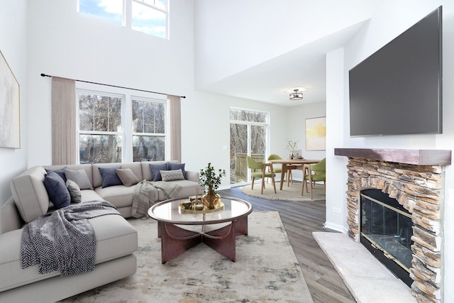 living room featuring baseboards, a fireplace, a high ceiling, and wood finished floors