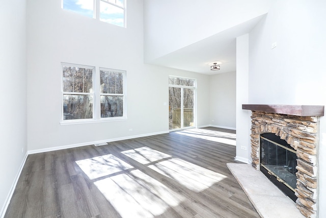 unfurnished living room with visible vents, baseboards, wood finished floors, a high ceiling, and a stone fireplace