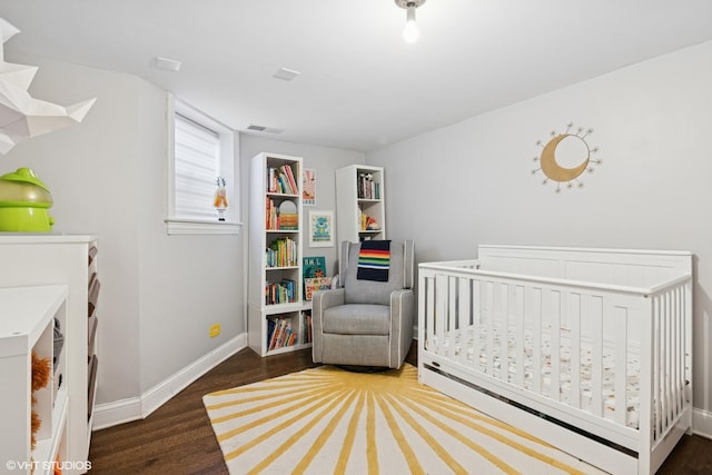 bedroom with a crib, baseboards, visible vents, and wood finished floors