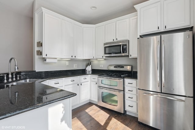 kitchen with dark wood finished floors, dark stone countertops, appliances with stainless steel finishes, white cabinets, and a sink