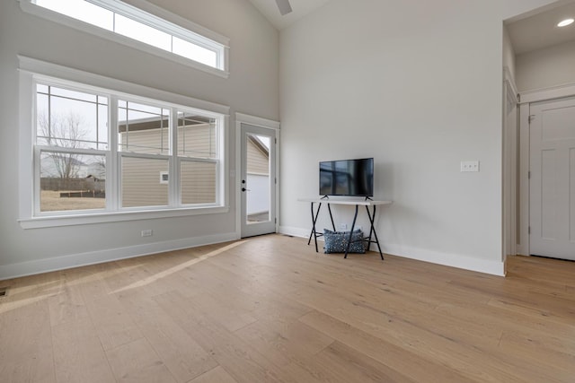 unfurnished living room featuring a towering ceiling, baseboards, wood finished floors, and recessed lighting