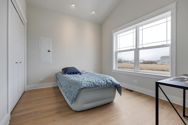 bedroom featuring electric panel, visible vents, baseboards, lofted ceiling, and light wood-style flooring