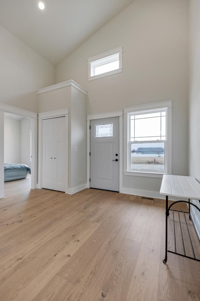 foyer with light wood finished floors, high vaulted ceiling, and a wealth of natural light