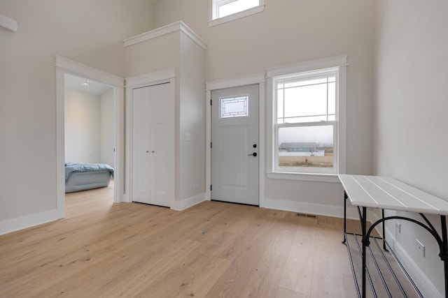 entryway featuring light wood-style floors, visible vents, a towering ceiling, and baseboards