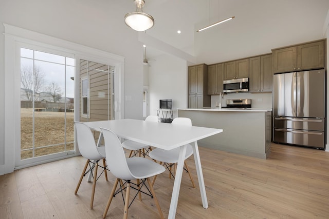 dining room with a towering ceiling, light wood-style floors, and recessed lighting