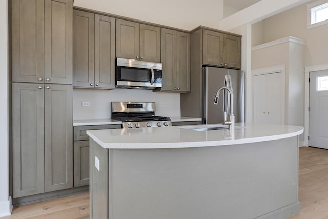 kitchen with a center island with sink, appliances with stainless steel finishes, light countertops, light wood-type flooring, and a sink