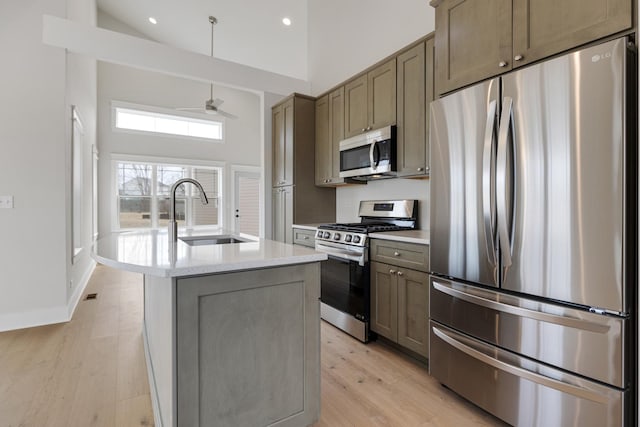 kitchen with a center island with sink, appliances with stainless steel finishes, light wood-style floors, high vaulted ceiling, and a sink