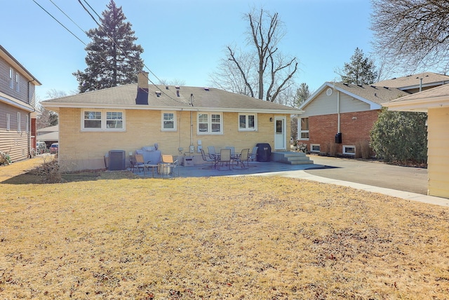 rear view of house featuring a patio area, a chimney, a lawn, and brick siding