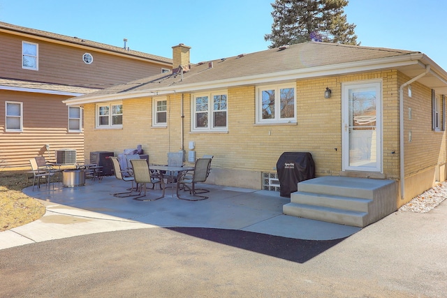 back of property with a patio, brick siding, a chimney, and central AC unit