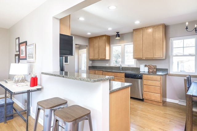 kitchen featuring dishwasher, a breakfast bar area, a sink, and light wood-style flooring