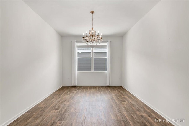 spare room featuring dark wood finished floors, baseboards, and an inviting chandelier