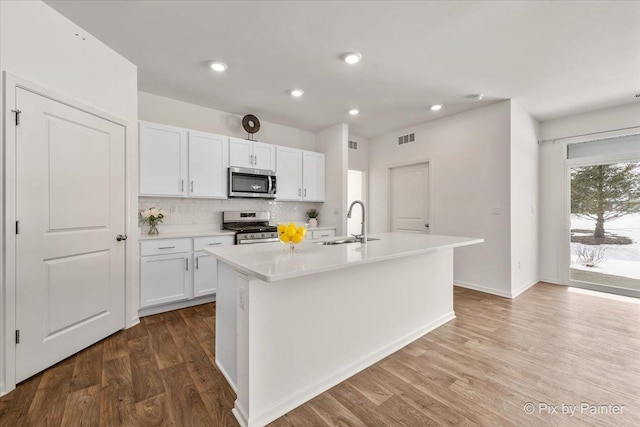 kitchen featuring stainless steel appliances, a sink, white cabinets, light countertops, and an island with sink