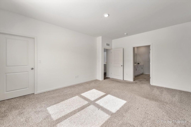 unfurnished bedroom featuring baseboards, ensuite bath, visible vents, and light colored carpet