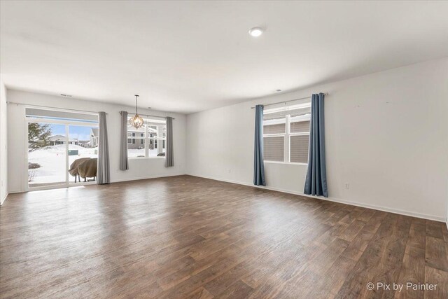 spare room with dark wood-style floors, baseboards, and an inviting chandelier