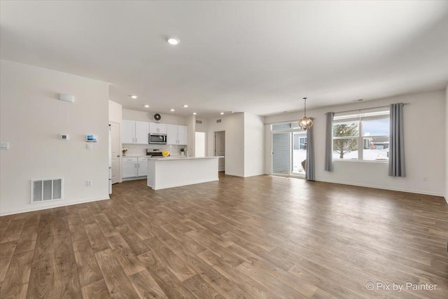 unfurnished living room featuring baseboards, visible vents, wood finished floors, a notable chandelier, and recessed lighting