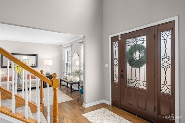 foyer entrance with stairs, ornamental molding, wood finished floors, and baseboards