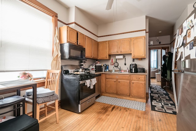 kitchen with black microwave, light wood-type flooring, brown cabinets, and stainless steel gas stove