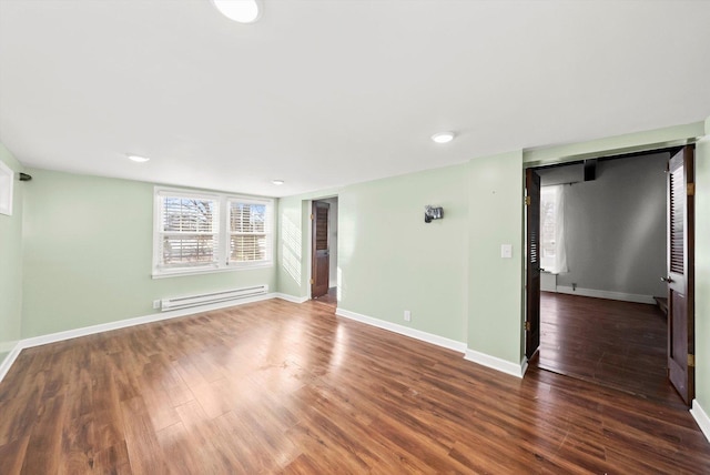 unfurnished room featuring a baseboard heating unit, baseboards, and dark wood-style floors