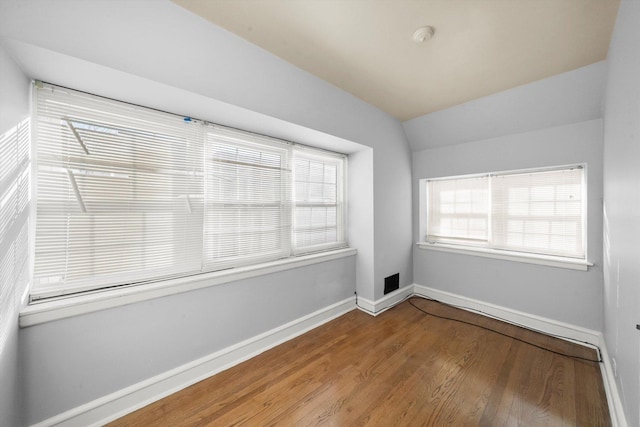 spare room featuring lofted ceiling, baseboards, and wood finished floors