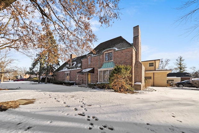 view of snowy exterior with brick siding and a chimney