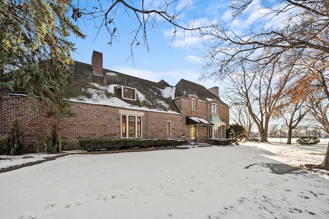 snow covered back of property with brick siding and a chimney