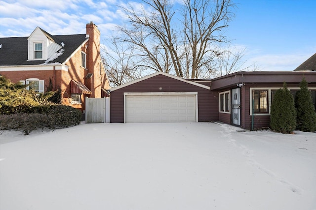 snow covered property featuring brick siding, a chimney, and an attached garage