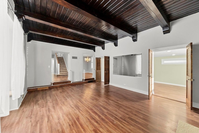 unfurnished living room featuring baseboards, wooden ceiling, stairway, wood finished floors, and beamed ceiling