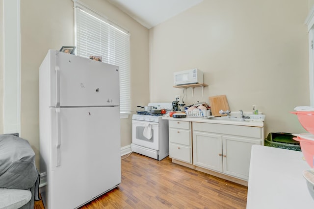 kitchen featuring light countertops, light wood-style flooring, white cabinetry, a sink, and white appliances