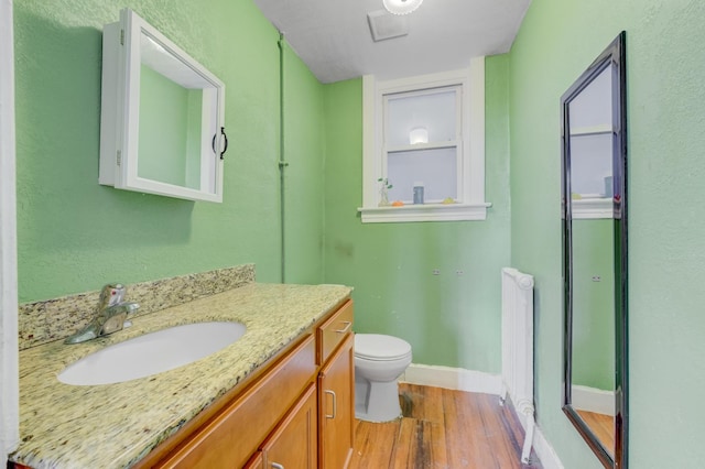 bathroom with visible vents, toilet, radiator, wood finished floors, and vanity