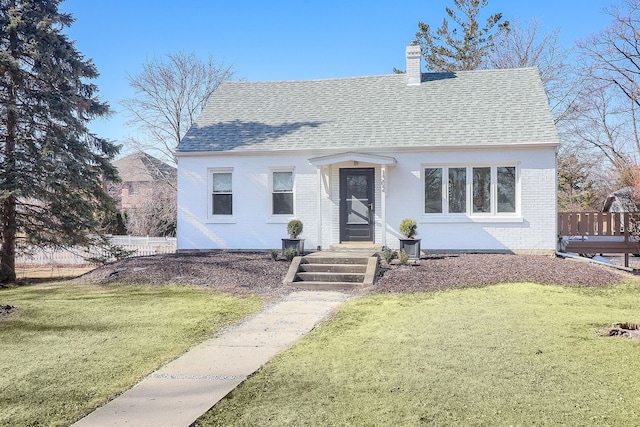 view of front facade with brick siding, a chimney, a front lawn, and roof with shingles