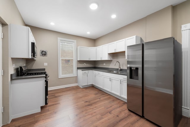 kitchen with stainless steel appliances, dark countertops, white cabinets, and a sink