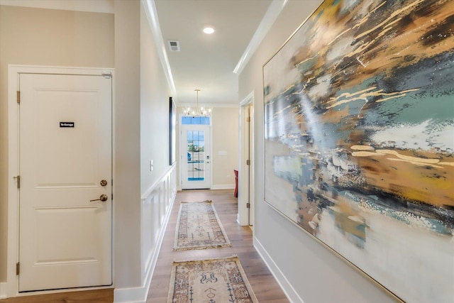 hallway featuring crown molding, visible vents, wood finished floors, a chandelier, and baseboards