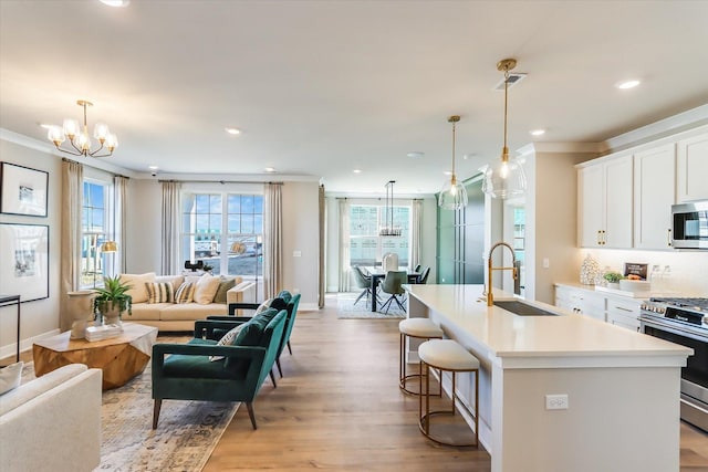 kitchen with appliances with stainless steel finishes, open floor plan, decorative light fixtures, a kitchen island with sink, and light countertops