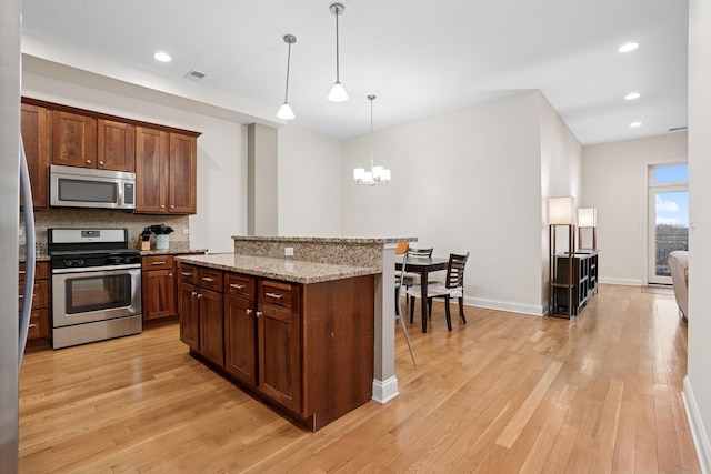 kitchen featuring hanging light fixtures, light stone countertops, stainless steel appliances, light wood-style floors, and backsplash