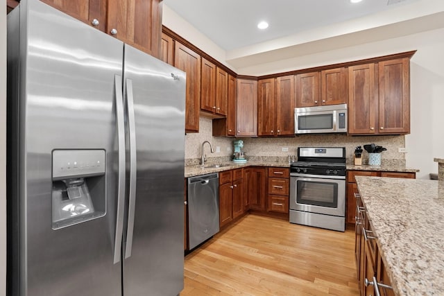 kitchen with tasteful backsplash, light stone counters, stainless steel appliances, light wood-style floors, and a sink