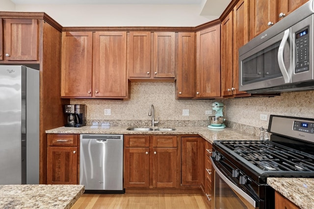 kitchen with light stone counters, appliances with stainless steel finishes, brown cabinets, and a sink