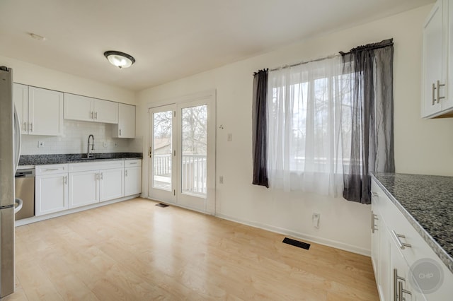 kitchen featuring visible vents, light wood-style flooring, decorative backsplash, white cabinets, and a sink