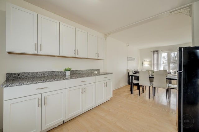 kitchen featuring light stone countertops, light wood-style flooring, white cabinets, and freestanding refrigerator