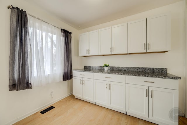 kitchen with light wood-style floors, visible vents, white cabinets, and dark stone countertops