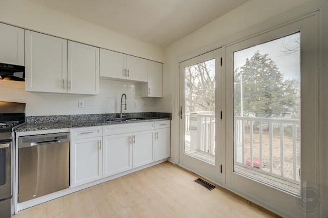 kitchen with visible vents, appliances with stainless steel finishes, dark stone countertops, white cabinetry, and a sink